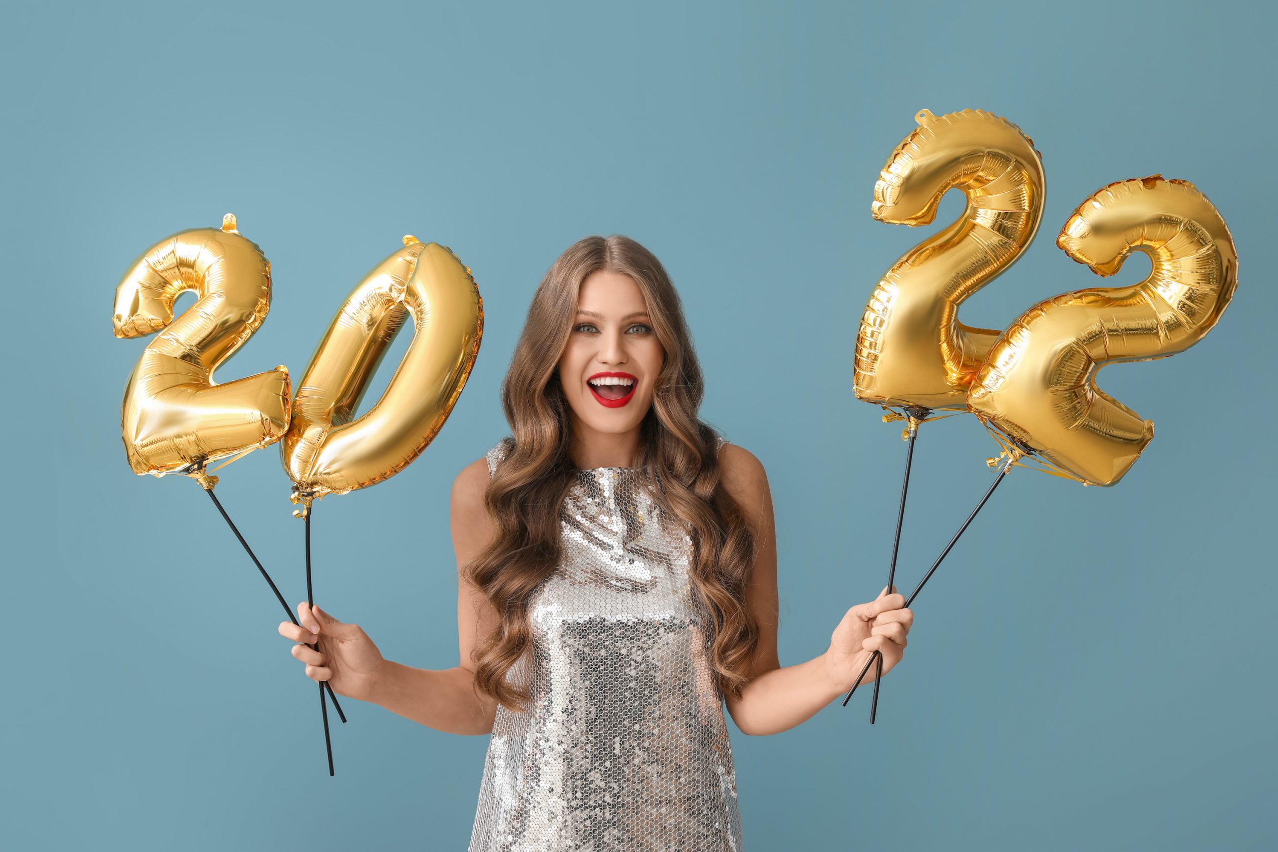 Beautiful young woman with balloons in shape of figure 2022 on blue background. New Year celebration; blog: Health Goals for the New Year