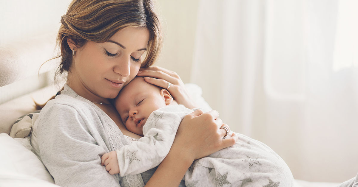 Loving mom carying of her newborn baby at home. Bright portrait of happy mum holding sleeping infant child on hands. Mother hugging her little 2 months old son; blog: How Does Public Health Benefit My Child?