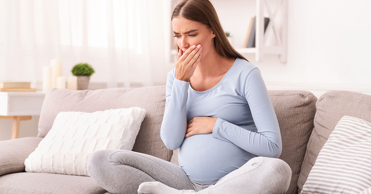 Morning Sickness. Pregnant Girl Feeling Sick Touching Mouth Sitting On Couch Indoor; blog: Regular Morning Sickness vs Hyperemesis Gravidarum