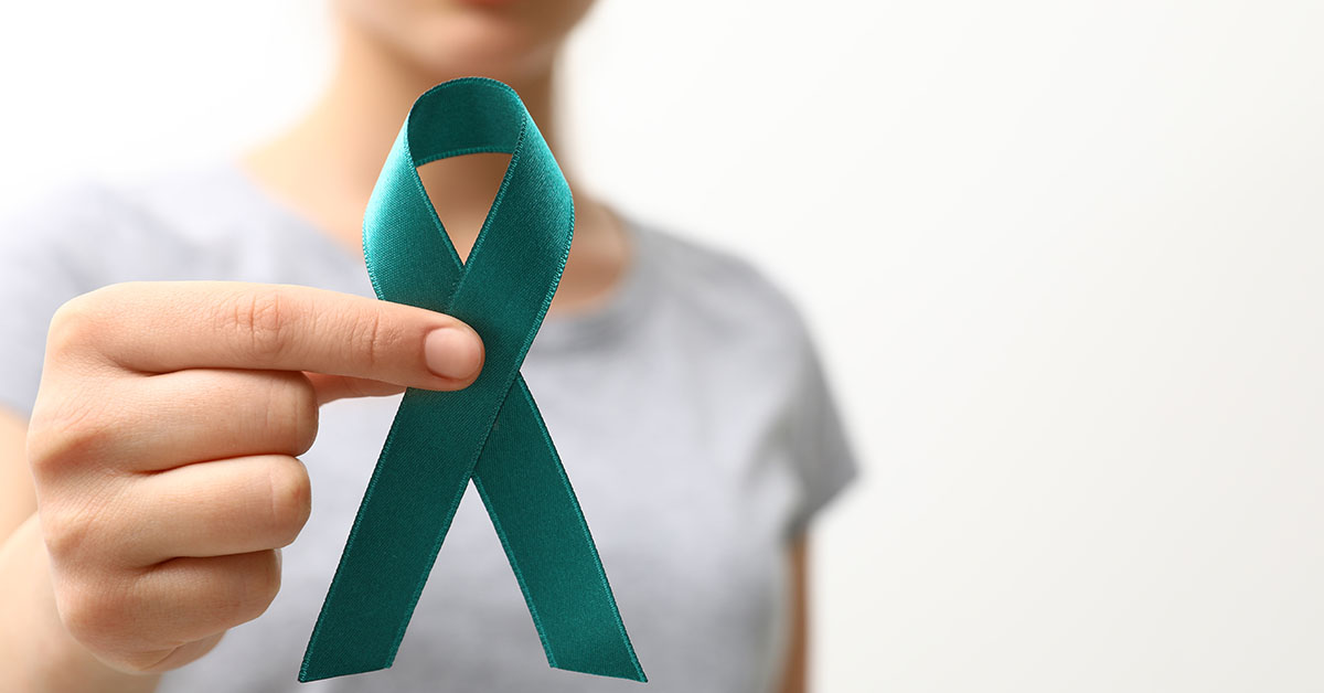 Woman holding teal awareness ribbon against light background, closeup; blog: Ovarian Cancer Diagnosis & Treatment